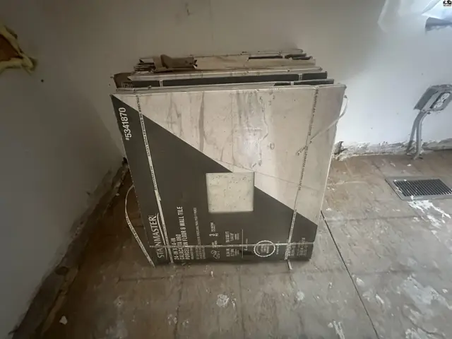Boxes of floor tiles are stacked in a room with unfinished walls and flooring.