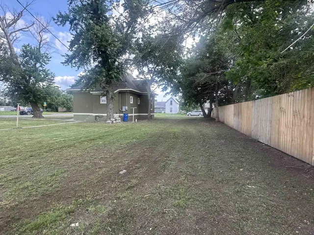 Exterior view of a green house with a new wooden fence and mature trees.
