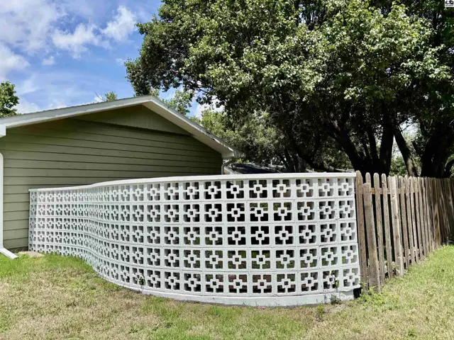 Curved white concrete block screen with decorative cutouts borders a green siding house and wooden fence.