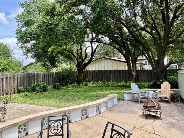Spacious backyard patio with concrete flooring, built-in seating, and mature trees.