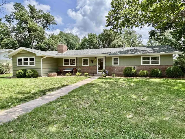 Exterior of a charming green ranch home with brick accents, large windows, and a well-maintained lawn.