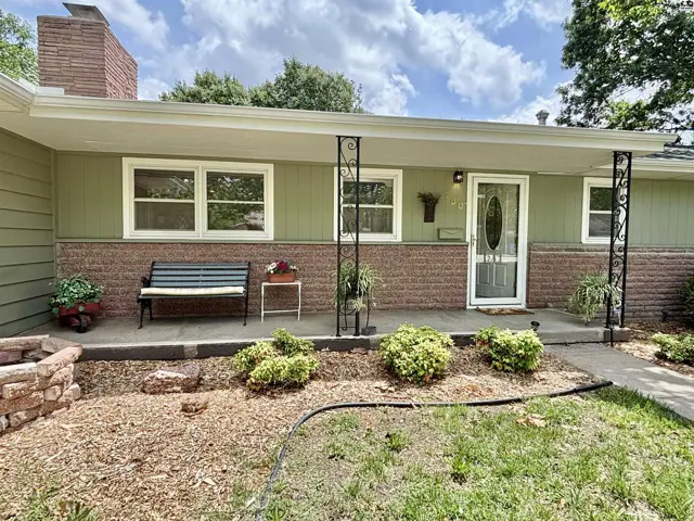 Exterior of a light green house with a brick accent, covered porch, and landscaping.