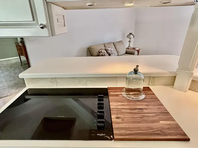Modern induction cooktop with butcher block cutting board and view of a living area with sofa.