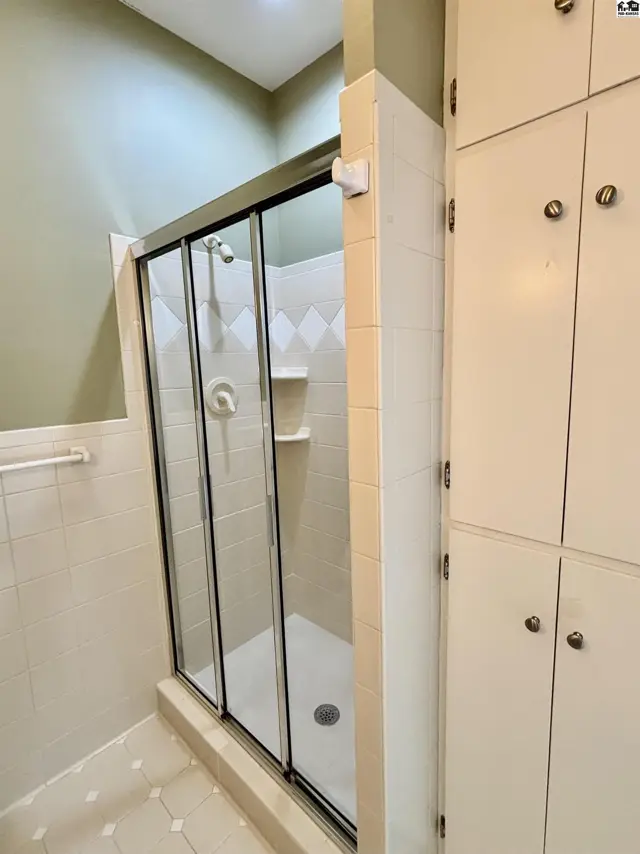 A bathroom features a sliding glass shower door, tiled walls, and tall cream-colored cabinets.