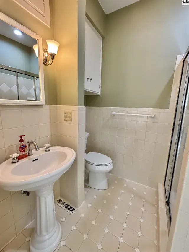 Bathroom with pedestal sink, tiled shower, and light green walls.