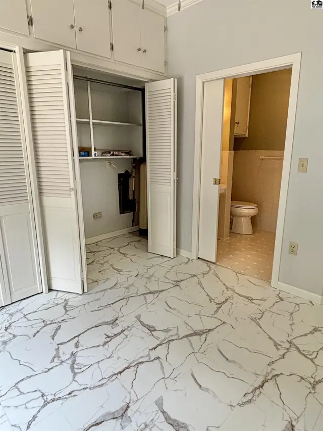 Spacious room with marble-look flooring, bi-fold closets, and an adjoining bathroom with a toilet.