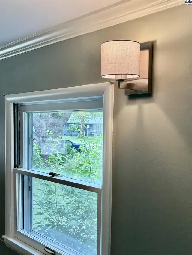 Modern wall sconce illuminates a room with a double-hung window and green walls.