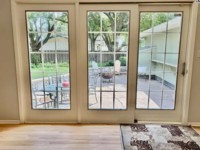 French doors open to a patio with outdoor seating and a fire pit, surrounded by trees.