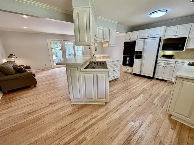 Spacious white kitchen with a central island, stainless steel appliances, and light wood floors.