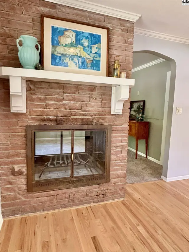 Rustic stone fireplace with a wooden mantel and glass doors, adjacent to a hallway with hardwood floors.