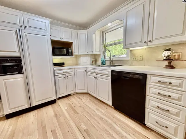 Bright white kitchen with light wood floors, granite countertops, and stainless steel appliances.