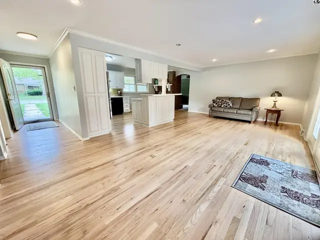 Spacious living room with hardwood floors, white cabinets, and a view into the kitchen.