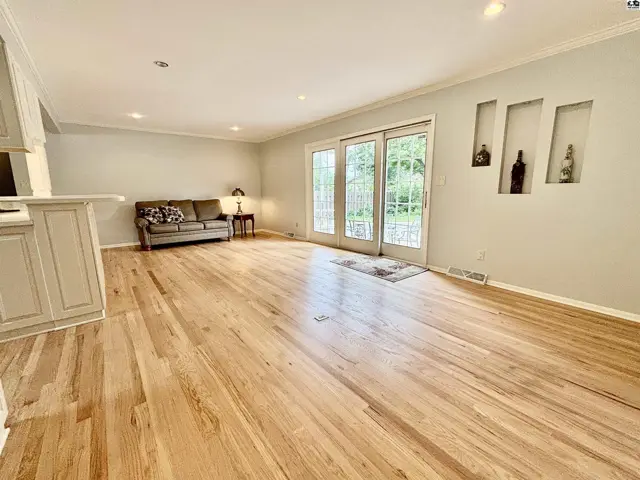 Spacious living room with light hardwood floors, neutral walls, and glass doors leading outdoors.