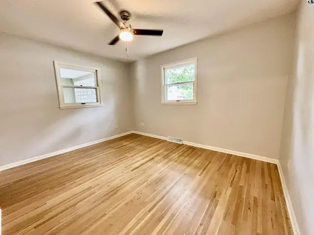Bright bedroom with polished hardwood floors, neutral walls, and two windows.