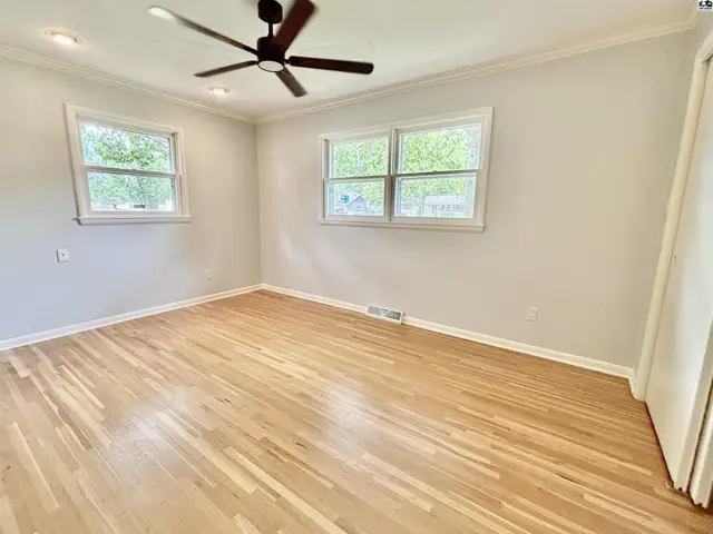 Spacious bedroom with light wood floors, neutral walls, and a ceiling fan.