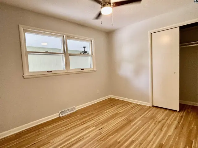 Bedroom with light wood floors, neutral walls, a ceiling fan, and a sliding closet door.