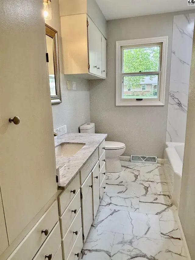 Modern bathroom with marble-look tile floors, vanity, and shower surround, plus a white toilet and tub.