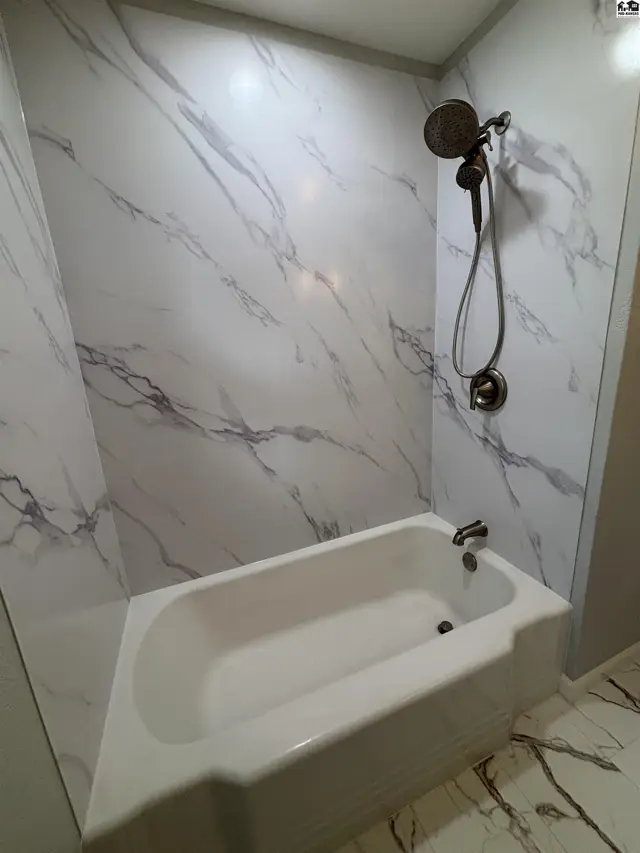 Modern bathroom features a white bathtub with marble-patterned walls and matching floor tiles.