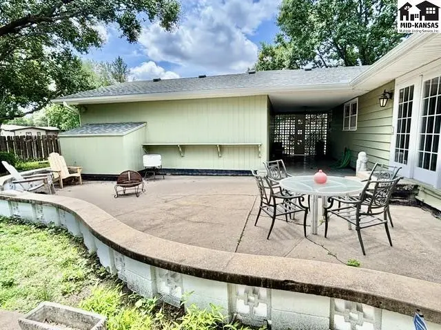 Spacious concrete patio with outdoor seating and a covered patio area, bordered by a low wall.