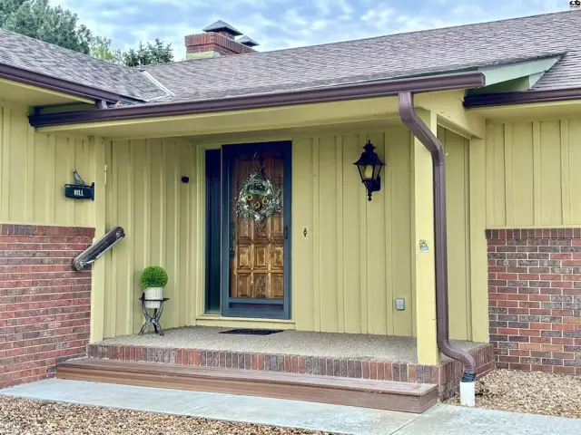 Covered front porch with wood door, brick accents, and yellow siding.