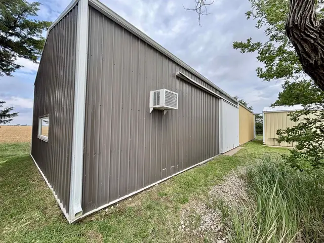 Exterior of a large, brown metal building with white trim, a sliding door, and an air conditioning unit.
