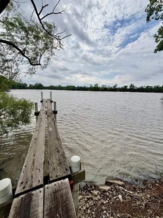 Wooden dock extends into a calm lake surrounded by trees under a cloudy sky.