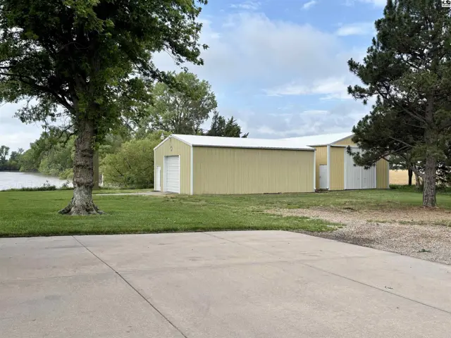 Expansive yellow metal outbuildings with white garage doors sit on a grassy lot near a body of water.