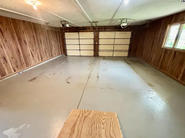 Spacious garage with wood-paneled walls, two overhead doors, and a painted concrete floor.
