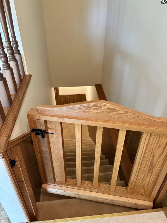 Wooden banister and gate frame a carpeted staircase leading down to a hallway.
