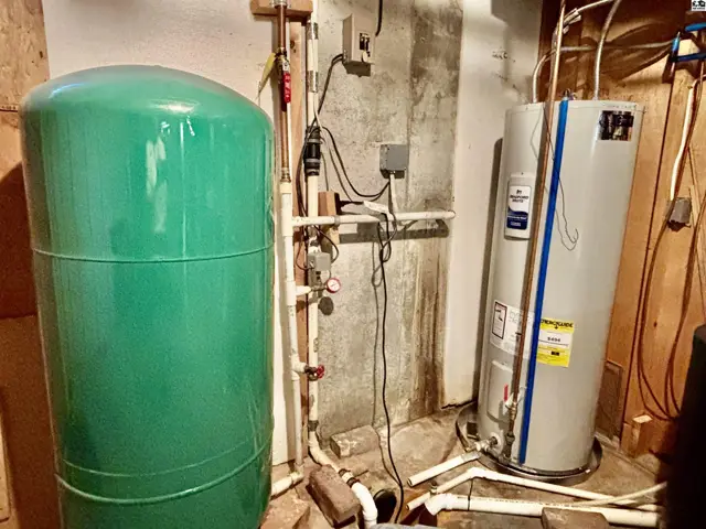 Basement utility area with a large green pressure tank and a tall water heater.