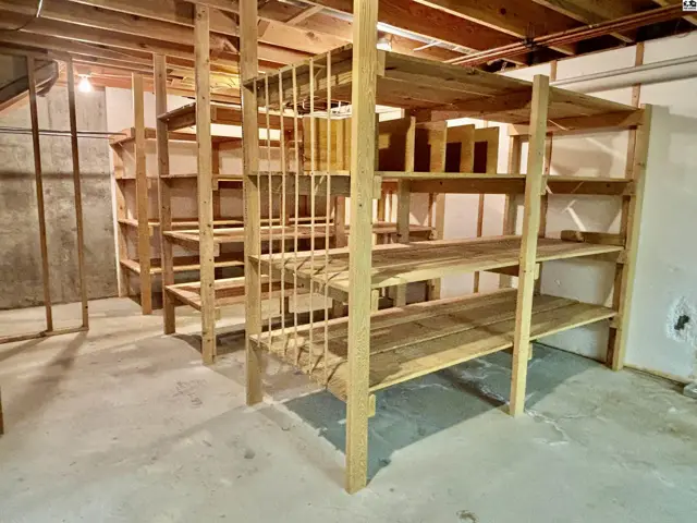 Spacious unfinished basement with extensive wooden shelving and concrete floor.