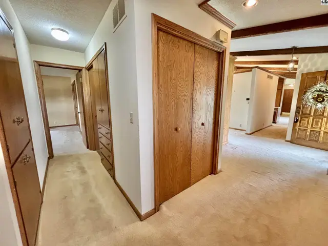 Hallway with plush carpet, wood-paneled doors, built-in cabinets, and exposed ceiling beams.