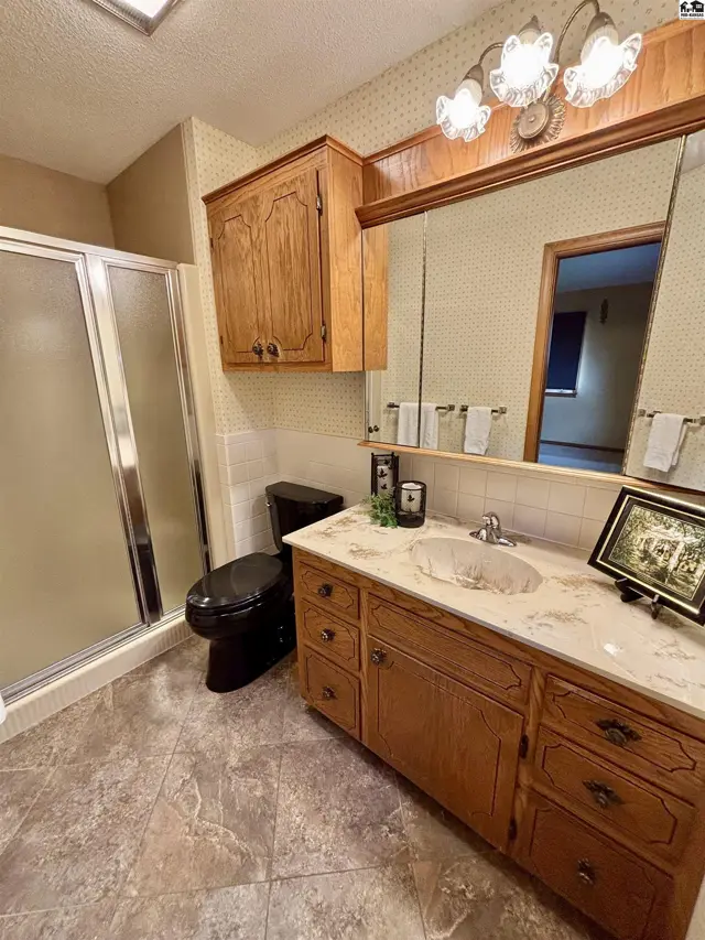 Spacious bathroom features a glass shower, black toilet, wood vanity, and marble countertop.