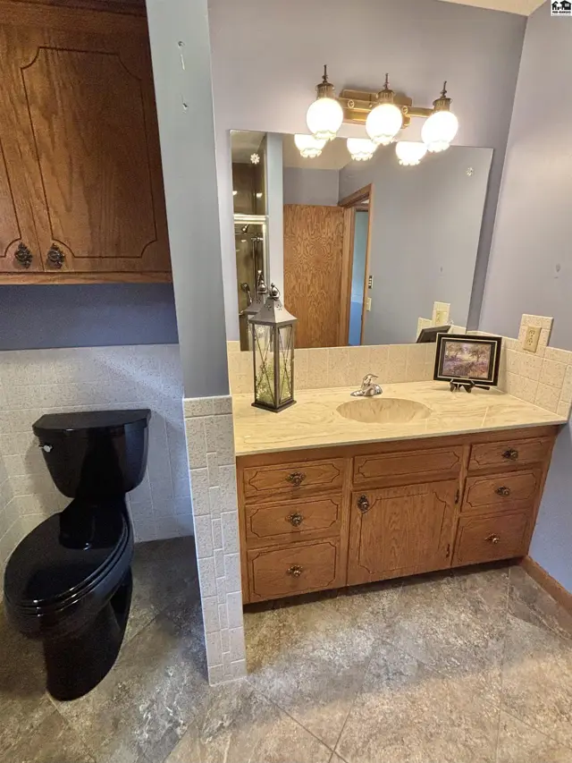 Spacious bathroom with a black toilet, light blue walls, and a double vanity with oak cabinets.