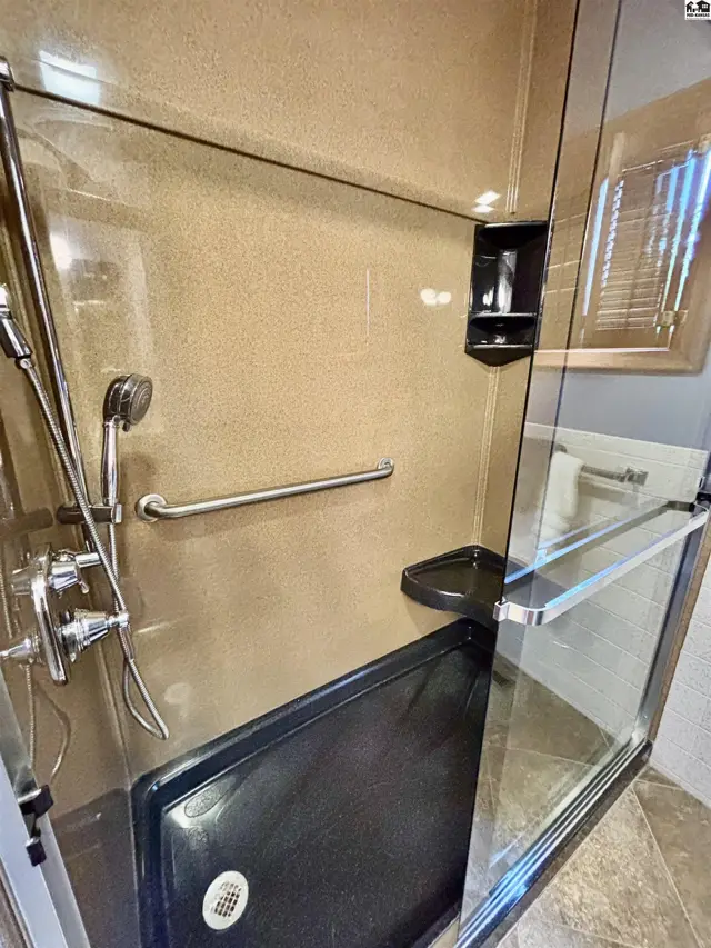 Spacious walk-in shower with textured walls, grab bar, and glass enclosure.
