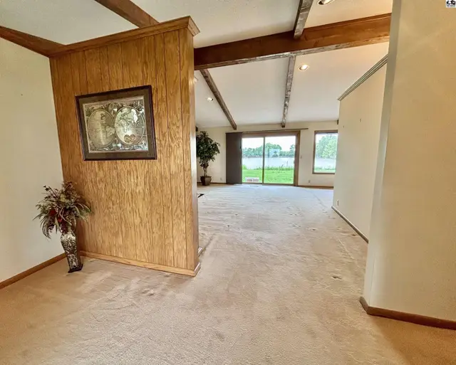 Spacious living area with wood-paneled accent wall, vaulted beamed ceiling, and large sliding doors to the backyard.