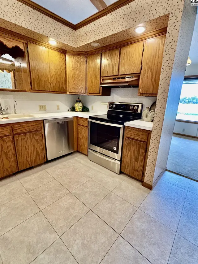 Warm oak cabinets, stainless steel appliances, and tiled floors in a well-lit kitchen.