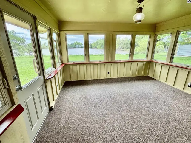 Sunroom with abundant windows overlooking a lake, featuring paneled walls and carpeted floors.