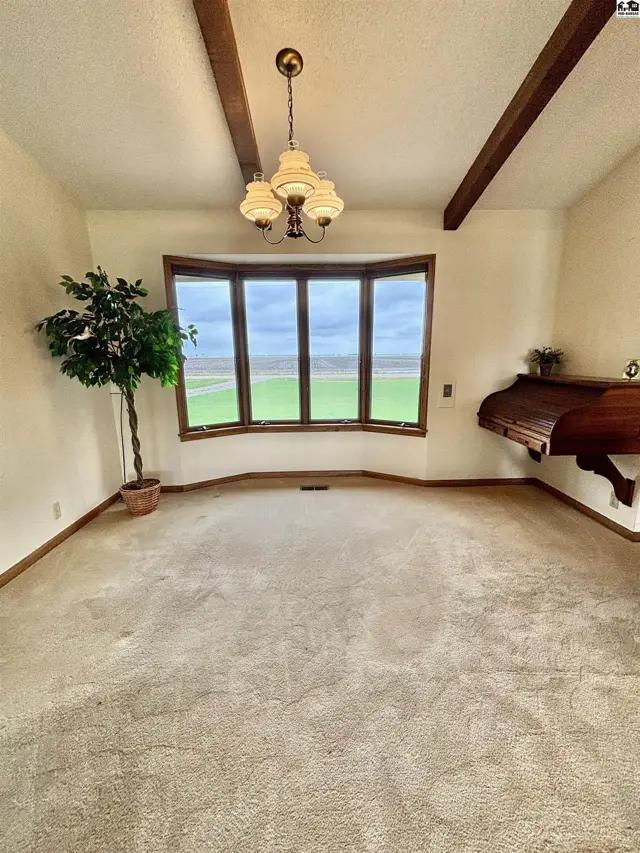 Spacious dining room with a bay window, carpet, wood beams, and a chandelier.