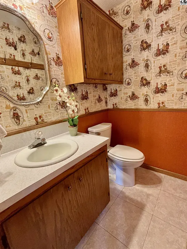 Powder room with a wood vanity, white sink, ornate mirror, and vintage-themed wallpaper.