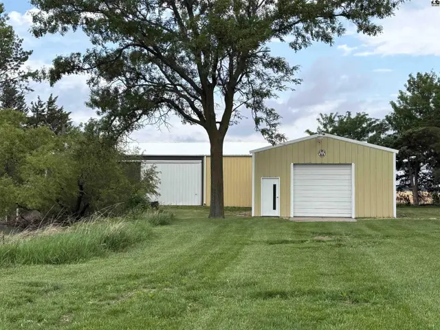 Exterior view of a tan metal garage with a white roll-up door and a white side door.