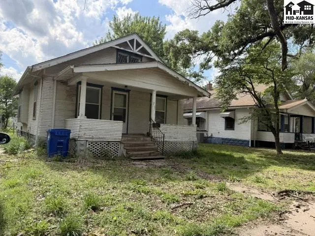 Charming bungalow with a covered front porch, white siding, and mature trees in the yard.
