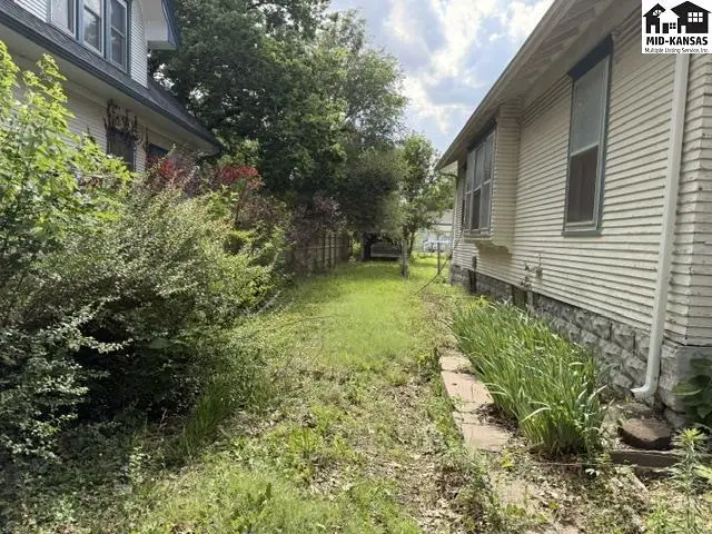 Exterior view of two houses with siding, stone foundation, and overgrown landscaping.