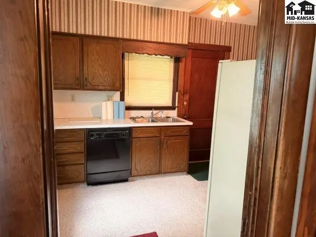 Kitchen with wood cabinets, white countertops, black dishwasher, and striped wallpaper.
