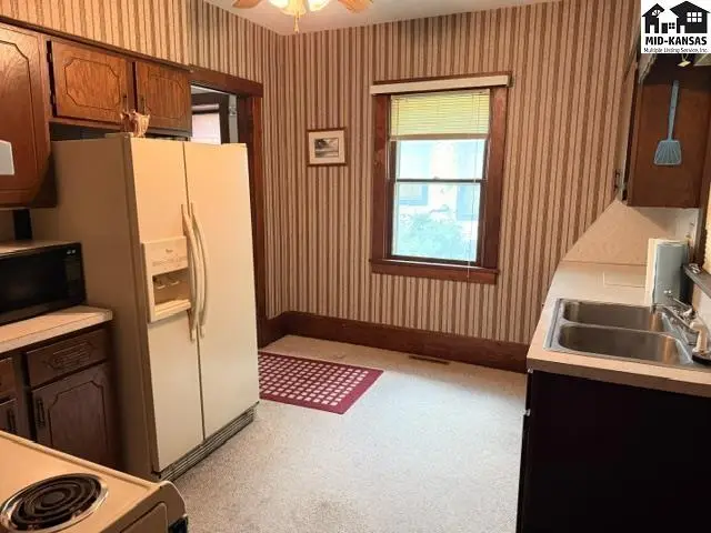 Kitchen with striped wallpaper, wooden cabinets, a double sink, and a large refrigerator.