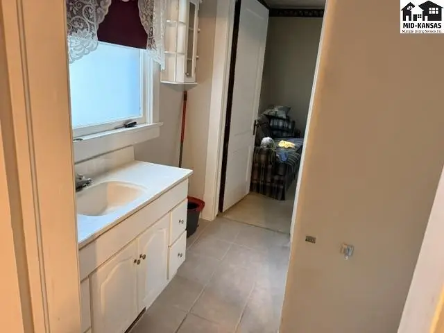 White vanity with sink and tiled floor in a bathroom, with a bedroom visible through an open doorway.