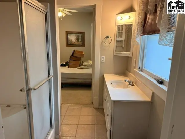 Bathroom with white vanity, marble countertop, and tiled floor, leading to a bedroom.