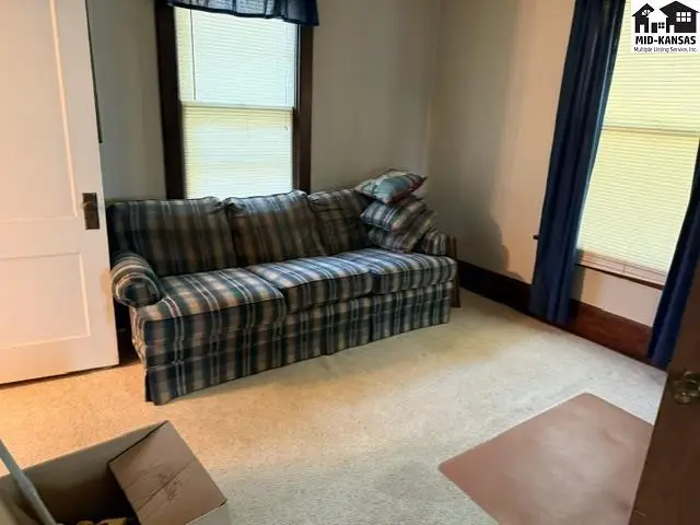 A plaid sofa sits in a carpeted room with large windows and dark wood trim.
