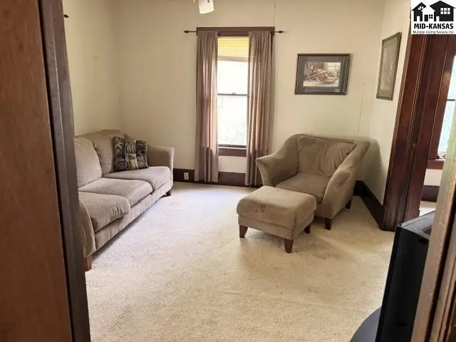 Living room with beige sofa, armchair, ottoman, and neutral carpet.
