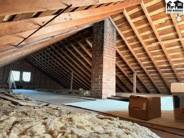 Attic space with exposed wooden beams, brick chimney, and unfinished flooring.